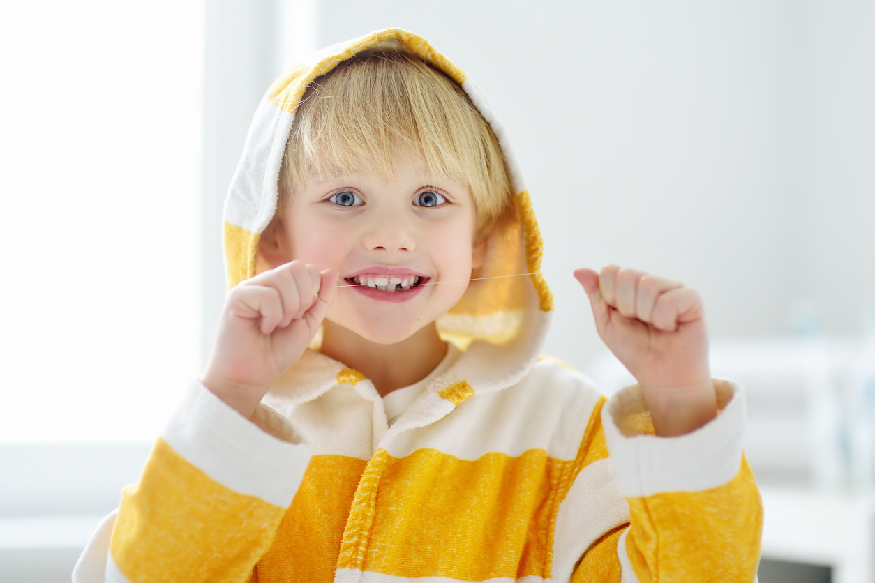 Young boy flossing his teeth and smiling while wearing a white and yellow striped bath robe.