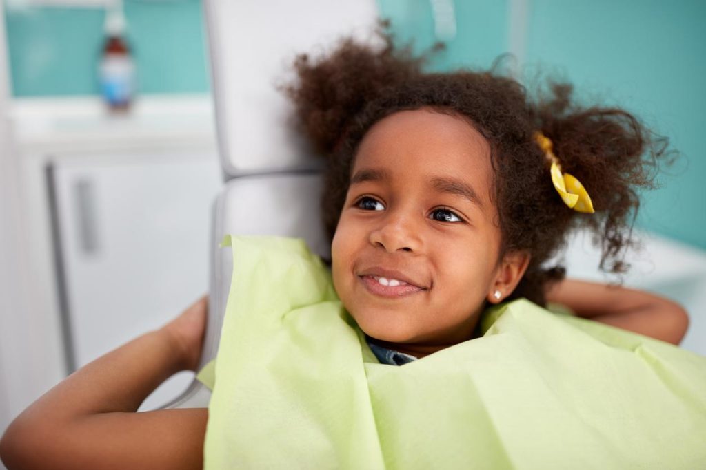 Little girl smiling in dentist chair with bib on for dentist appointment