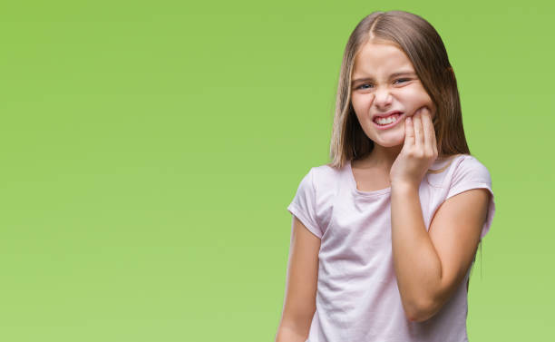 Young girl holding her jaw due to tooth pain with green background.