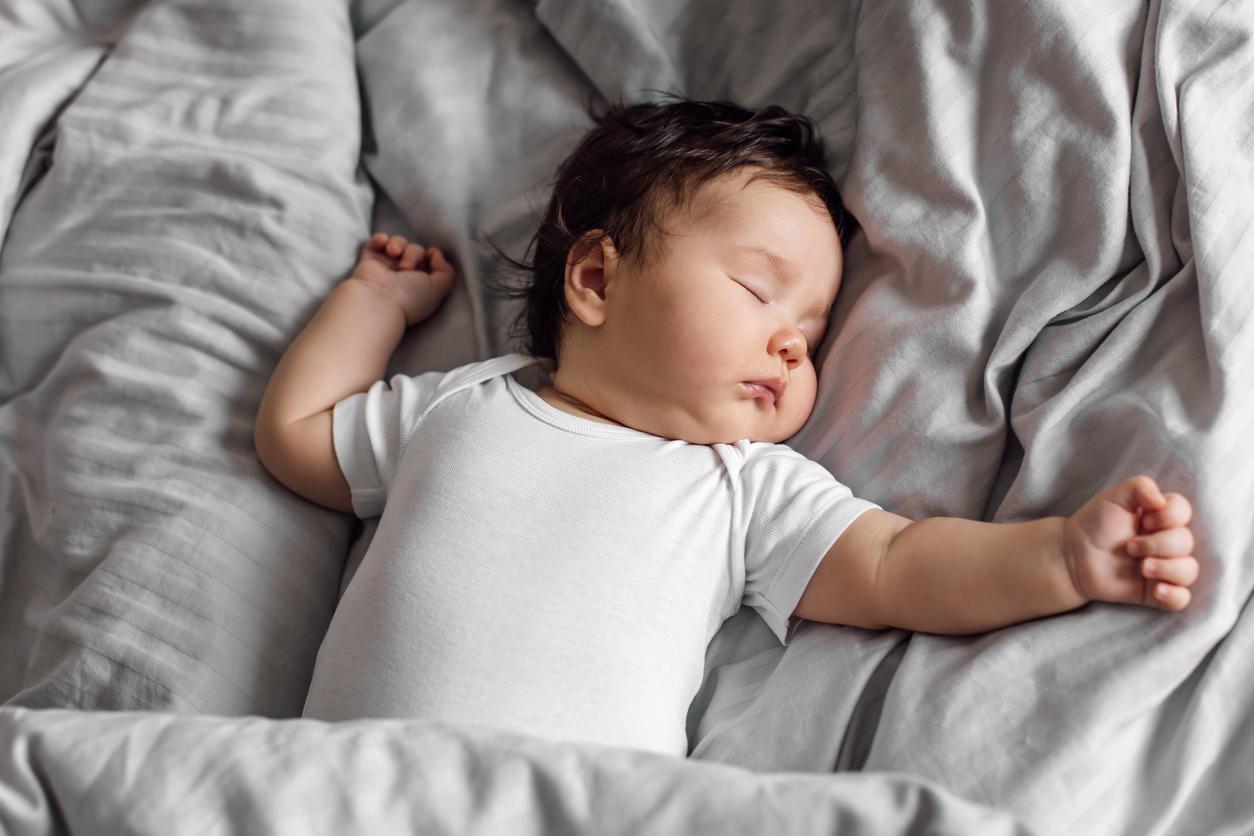 Baby in a onesie sleeping in a crib with their arms outstretched