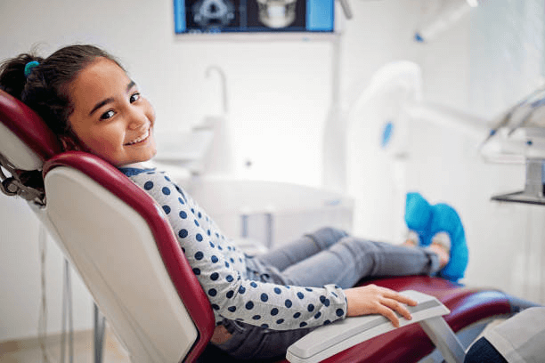 A young girl turning her head to smile at the camera while sitting in a dental chair.