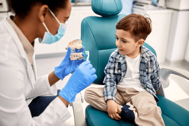 Female dentist showing a dental model to a little boy who is sitting in a dental chair.