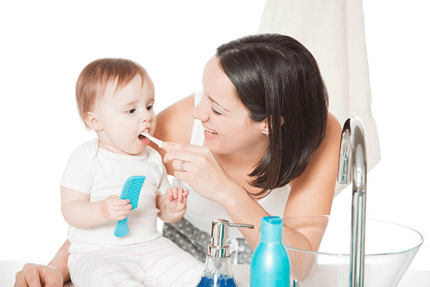 Mother brushing her child’s teeth with a small toothbrush at a bathroom sink.