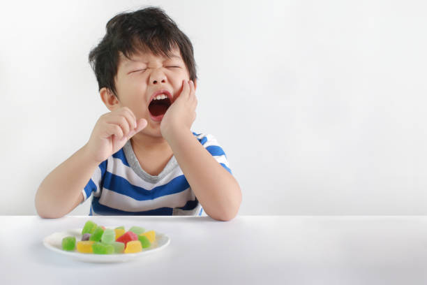 A child eating candy and holding his jaw in pain due to a toothache.