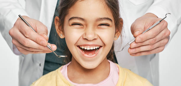 Regular dental check-up. Young girl smiling in front of a dentist who is holding dental instruments.